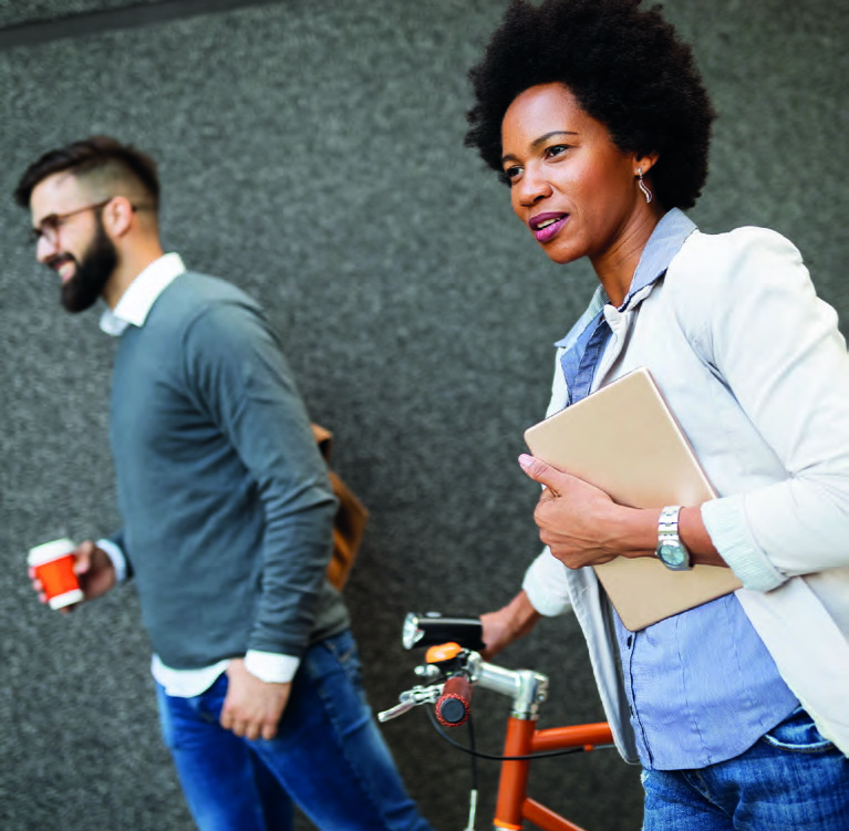 mittelalte, schwarze Frau in dynamischer Bewegung mit Dokumentenmappe unter dem Arm, schiebt ein orangenes Fahrrad, im Hintergrund ein Mann mit Bart und grauem Pullover, hält einen Kaffeebecher