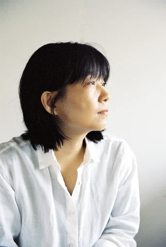 Frau mit schulterlangem, schwarzen Haar und Pony in weißer, lockerer Bluse, im Profil fotografiert