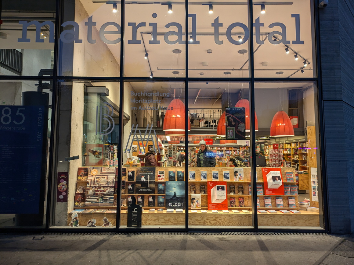 großes, in Elemente unterteiltes Schaufenster einer beleuchteten Buchhandlung mit großen roten Lampen, Umgebung dunkel