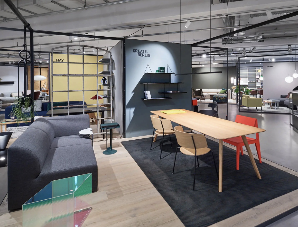 Blick in einen Einrichtungsladen, ein heller Holztisch mit Stühlen auf einem dunklen Teppich, links daneben ein dunkelgraues Sofa