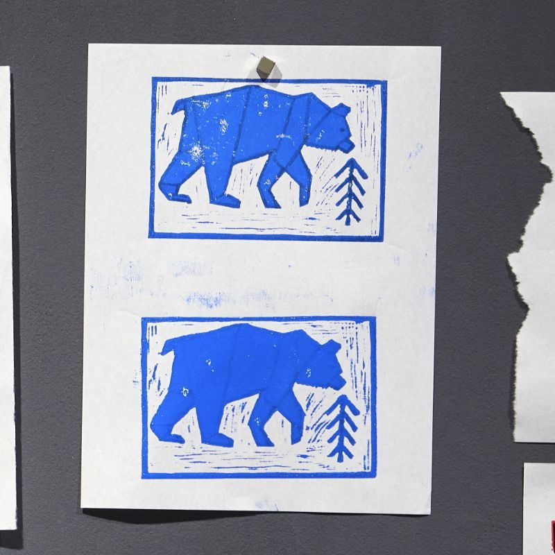 Linolschnitt, blauer Eisbär auf weißem Grund mit Rahmen und einem angedeuteten Bäumchen, zweimal auf ein Papier gedruckt