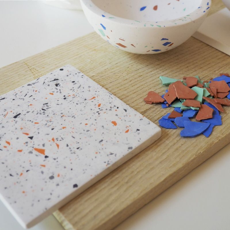 weiße Materialplatte mit bunten Sprenkeln, daneben bunte Plättchen, im Hintergrund ist ein Teil einer Terrazzo Schüssel zu sehen