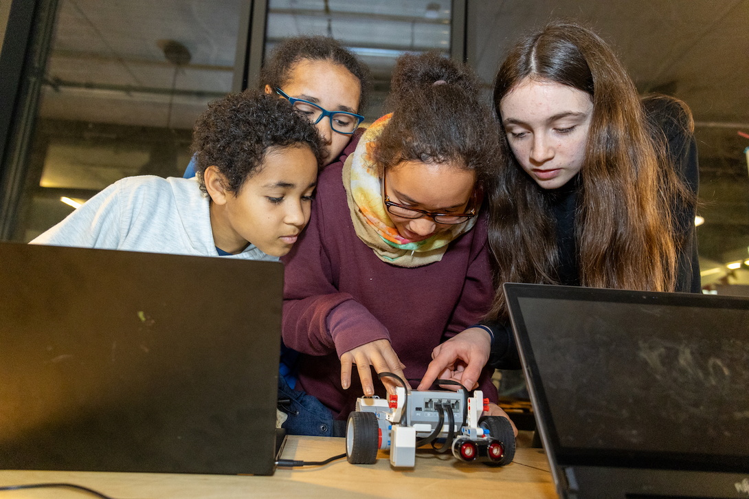 vier junge Mädchen beugen sich hinter zwei Laptops über ein Modellauto