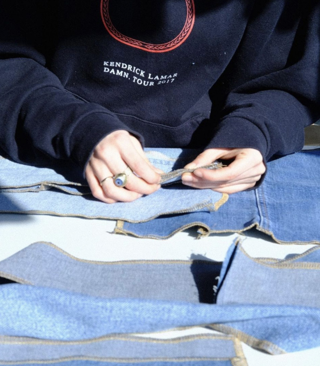 zierliche Hände, Arme in dunkelblauem Sweater, arbeiten mit Nadeln an Jeansstoffen, davon verschiedene auf einem Tisch