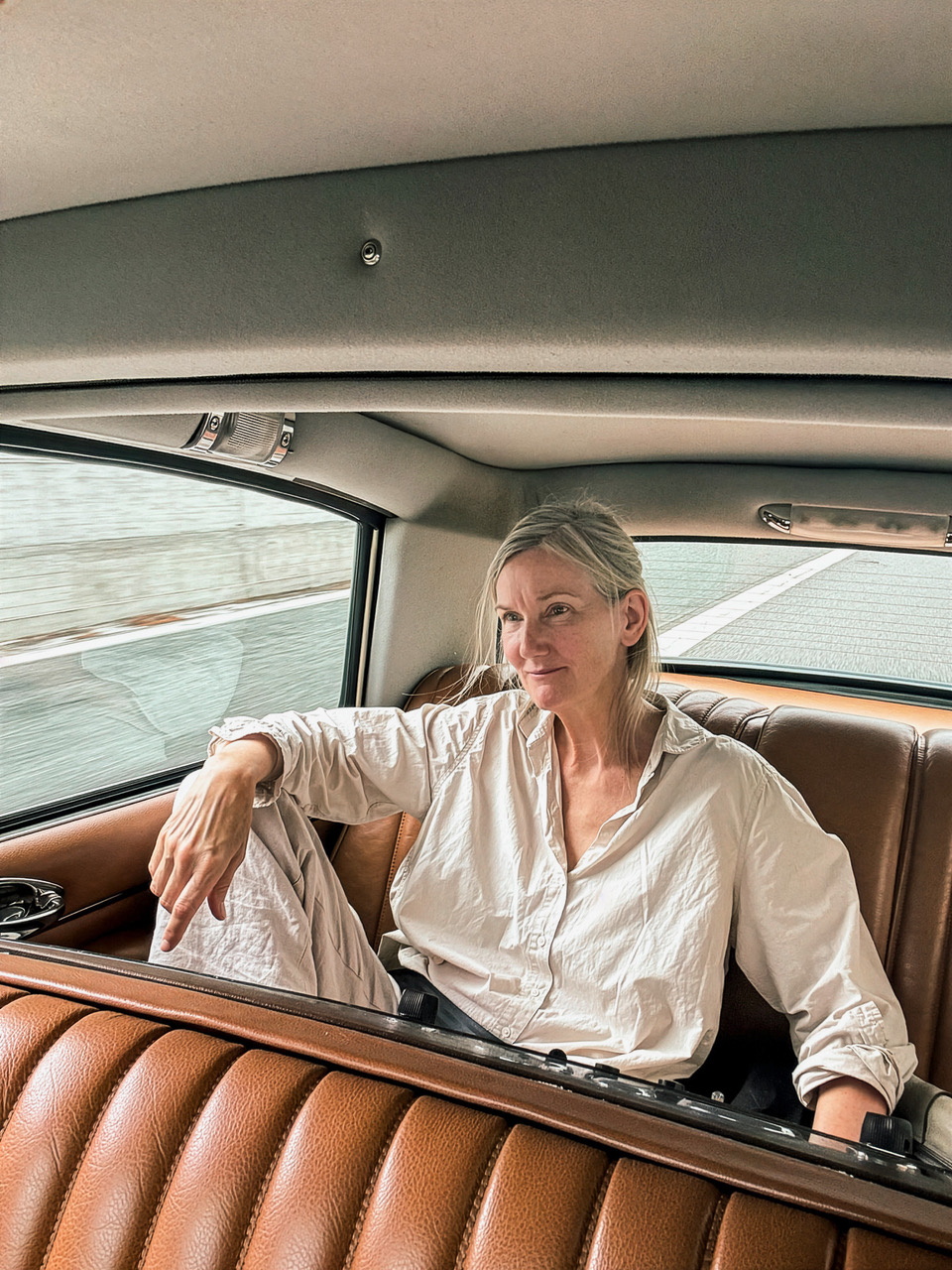 mittelalte weiße Frau mit schulterlangen grauen Haaren auf dem Rücksitz eines hellen Autos mit rotbraunen Ledersitzen